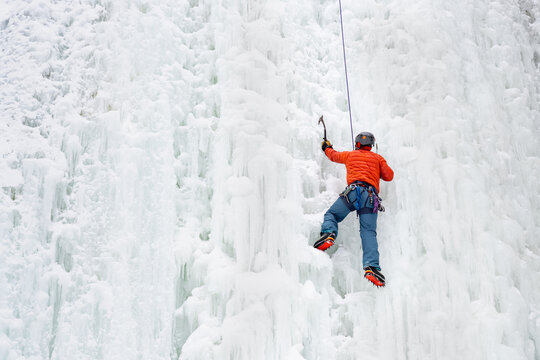 Man Ice Climbing a Frozen Waterfall in Winter with Ice Axe