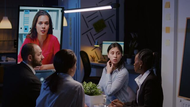 Workaholics diverse multi-ethnic teamwork having online videocall conference meeting overworking at financial strategy in office room late at night. Focused teamwork discussing company ideas in