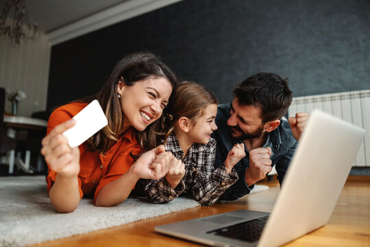Happy family using laptop for online shopping. They are excited for purchase. Mom holding credit card.