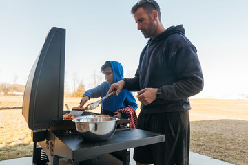 Dad teaching son how to grill outside. 