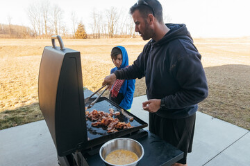 Dad teaching son how to grill outside. 