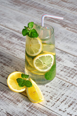 Cold lemonade in a glass and fruit on an old wooden table. Summer refreshing drink. Cold water for detoxification with lemon and mint