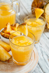 Tasty pineapple juice in two glasses with pineapple slices. Fresh natural pineapple cocktail and juice in Glass Jug on white wooden table