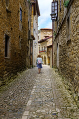 Fototapeta na wymiar Woman from behind walking through a narrow alley with old stone houses. Santilla del Mar.
