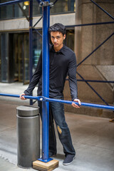 Dressing in a black shirt, a fashionable pants, a young asian teenager is holding on construction frames and looking at you...