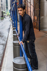 Dressing in a black shirt, a fashionable pants, a young asian teenager is holding on construction frames and looking at you..