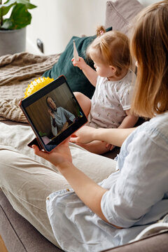 Doctor consulting mother with baby via video chat on tablet