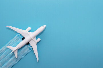 Plane model and medical mask on a blue background with copy space. Safe travels concept. Safety flight and travel during quarantine and lockdown