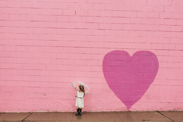 Landscape portrait of little girl in front of pink heart wall