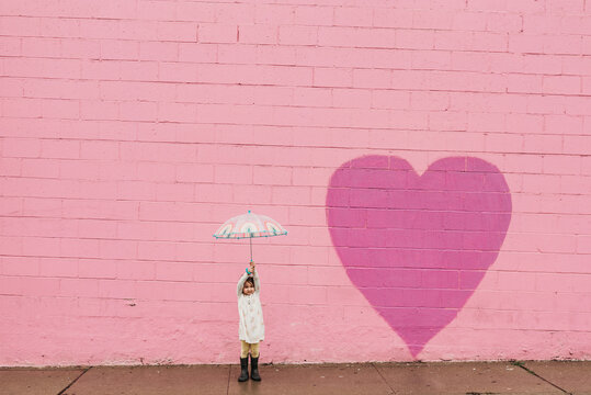 Little girl with umbrella in front of pink wall