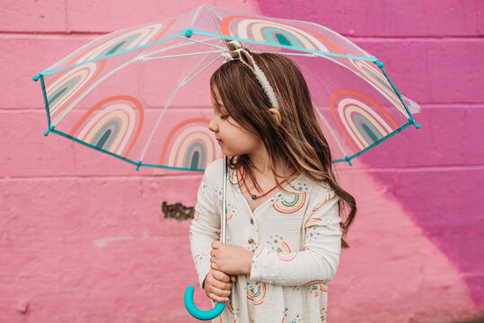 Beautiful child holding rainbow umbrella in the rain