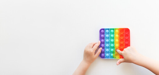 Children's hands hold a silicone toy pop it top view. The child plays an anti-stress game, simple dimple. Banner with copy space.