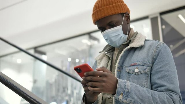 Professional Shopper In Disposable Face Mask Types On Orange Smartphone Standing On Escalator In Department Store Closeup