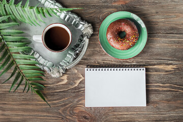 Fototapeta na wymiar Coffee break in a cafe for inspiration. A break during work. Blank notepad, coffee cup and donut on a wooden table. Place for text, advertising background.