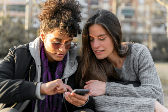Two young woman smiling and checking their smartphones.