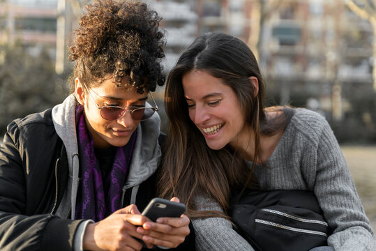 Two young woman smiling and checking their smartphones.