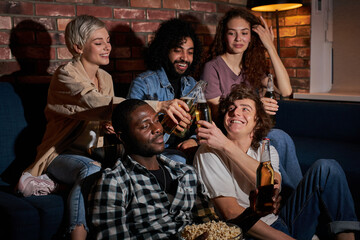 Joyful friends sitting at home and watching football game on television. Their favorite team is winning, victory concept. Cheering, drinking beer, having rest