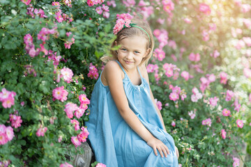 Summer portrait of pretty little girl wearing white dress and hat, posing in rose garden