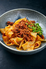 Modern style traditional Italian ragu alla bolognese sauce with papedelle pasta noodles and parmesan cheese served as close-up in a ceramic design bowl