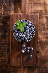 Bowl of fresh blueberries on rustic wooden board. Organic food blueberries and mint leaf for healthy lifestyle.