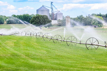 A rolling irrigator on a sod farm watering the grass with a grain leg and an old silo in the...
