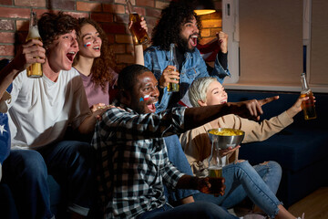 Group of friends watching sport competition on TV together, yelling and screaming by happiness, cheering at home in dark room at night