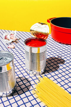 Tomato can and pasta over a checkered tablecloth with a yellow background