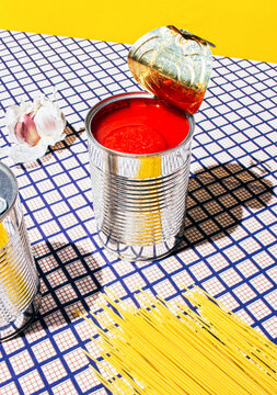 Tomato can, garlic and pasta over a checkered tablecloth with a yellow background