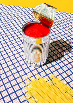 Tomato can and pasta over a checkered tablecloth with a yellow background