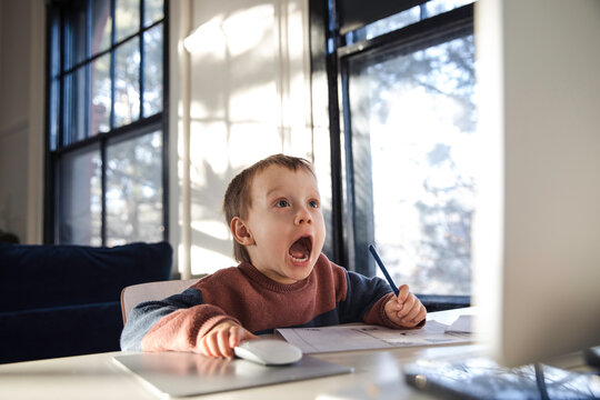 Little boy looking surprised while using desktop compute and a mouse
