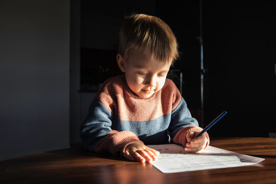 Little Boy Writing With Pencil On Paper In The Evening