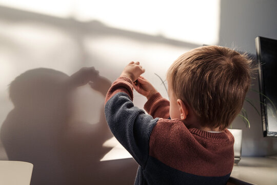 Little boy playing sun shadows on the wall
