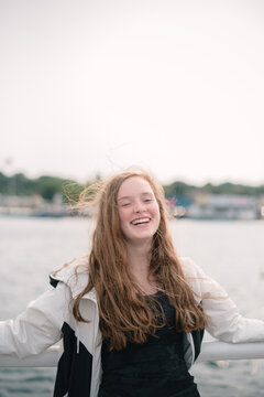 Teenage girl laughs happily beside the water.