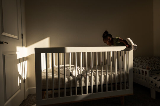 A toddler climbs into her crib