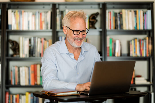 Older Man Laughs While Working on His Laptop at Home 