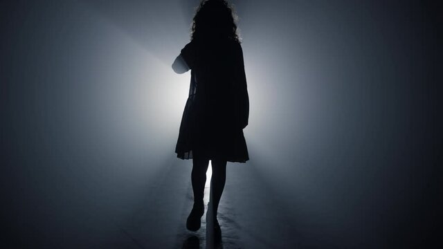 Silhouette woman walking in darkness. Girl walking in floodlight background.