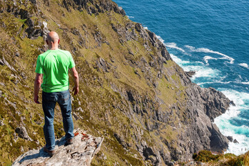Bald male tourist standing on the edge of a cliff, Beautiful scenery in the background. Warm sunny...
