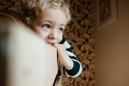 Toddler boy laying down in his bed and looking outside of the window