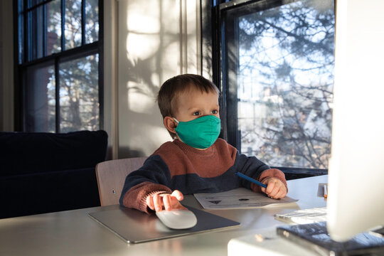 Little boy in face mask using desktop computer