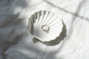 Engagement ring in shell-shaped jewelry plate on textured linen background