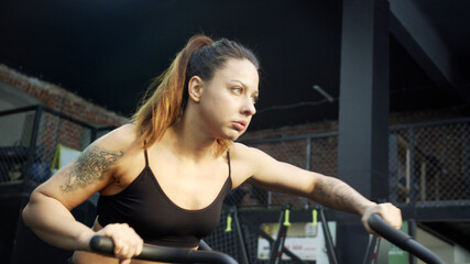 Fototapeta na wymiar A strong sportswoman is exercising on an exercycle hard