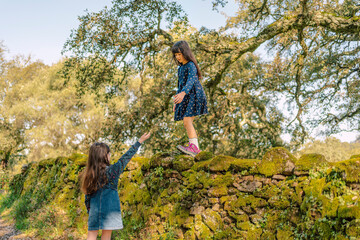 Girls helping each other down from a mountain of stones at field