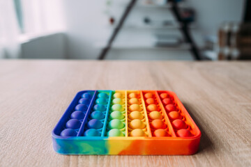 Naklejka premium Pop it into a rainbow-colored square lying in the center of the table in close-up. Popular toy. Antistress.