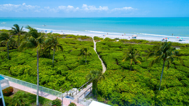 Beach in Sanibel Island, Florida with a wooden walkway going through dense vegetation to the sand