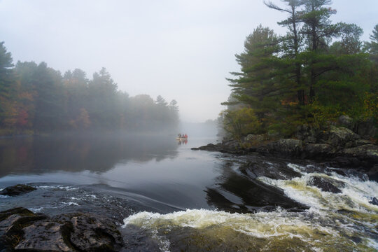 Canoe Paddling out of Mist Towards Dangerous Whitewater Rapids o