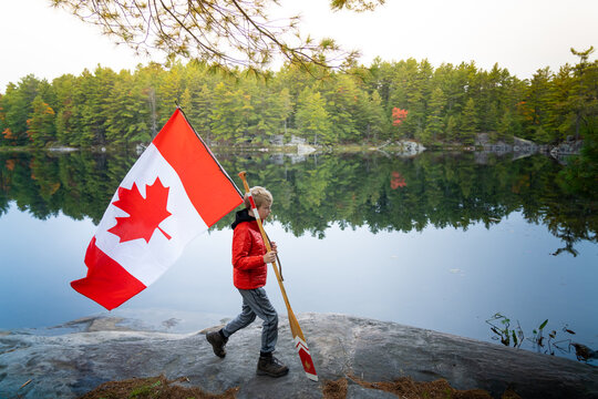 Boy Walking With Canadian Flag and Paddle in Back Country 