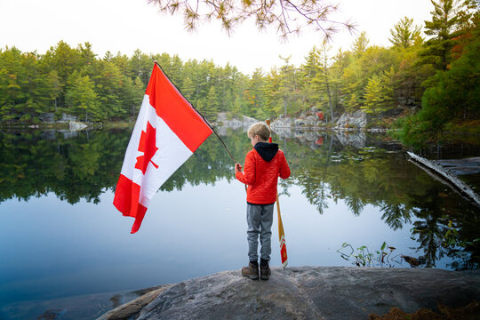 Boy Holding Canadian Flag and Paddle in Back Country