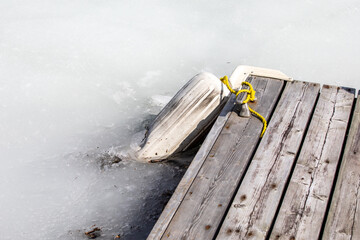 Fototapeta premium Bouée blanche prise dans la glace avec la glace d'un lac qui fond avec quai en bois