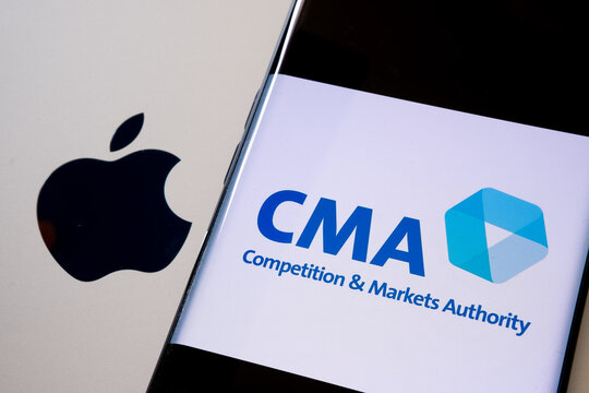 Apple logo on macbook surface and blurred UK CMA Competition and Markets Authority logo seen on the smartphone screen.  Concept. Stafford, United Kingdom, June 15, 2021.