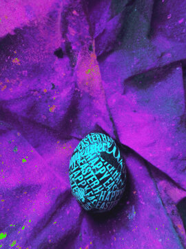 Colorful easter egg with a blue cast on a abstract purple background with copyspace